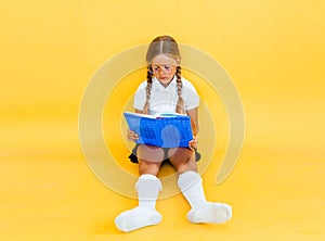 Cute little girl studying and reading a book while sitting on yellow background - education concept