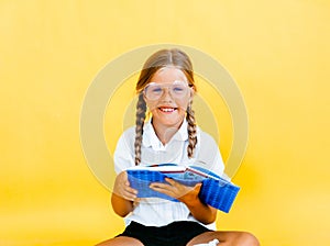 Cute little girl studying and reading a book while sitting on yellow background - education concept