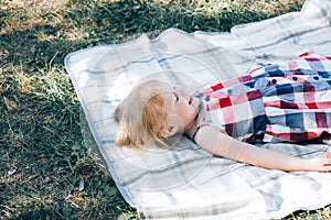 Cute little girl in a summer plaid sundress. Child lies on a light blanket on the grass