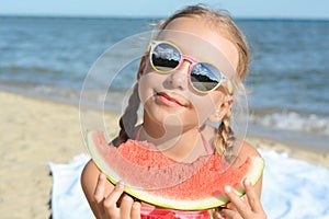 Cute little girl with sunglasses eating juicy watermelon on beach