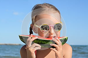 Cute little girl with sunglasses eating juicy watermelon on beach, closeup