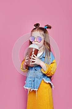 Cute little girl in sunglasses with glass jar of cocktail chilling on pink background
