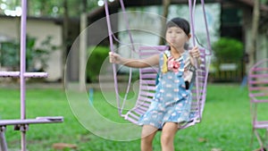 Cute little girl swinging in the playground with a smile and laughter. Active summer leisure for kids.