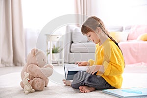 Cute little girl with teddy bear reading book on floor