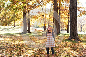 Cute little girl throwing autumn leaves at the park