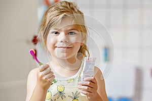 Cute little girl with a toothbrush and toothpaste in her hands cleans her teeth and smiles. Happy preschool child