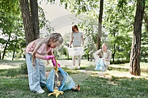 Cute little girl with trash bag collecting garbage while cleaning with parents in the park or forest