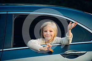 Cute little girl traveling in the car and observing nature from open window. Little girl waving hand for good bye in the