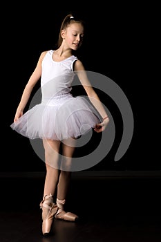 Cute little girl in a tutu and pointe shoes is dancing in the studio on a black background.