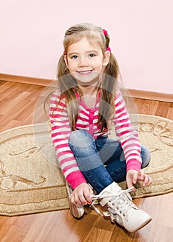 Cute little girl tying her white shoes at home