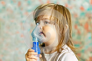 A cute little girl is undergoing medical inhalation treatment with a nebulizer at home. The girl is sitting and doing cough treatm