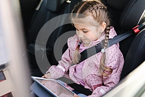 Cute little girl use tablet in car seat on the way to the kindergarten