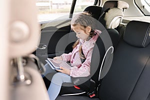 Cute little girl use tablet in car seat on the way to the kindergarten