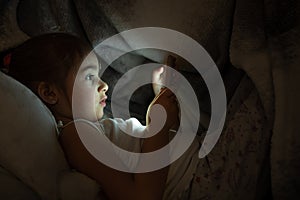 Cute little girl uses phone in bed at night instead of sleeping close up