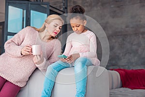 Cute little girl using her blue smartphone sitting near mother