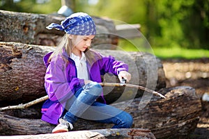 Cute little girl using a pocket knife to whittle a stick for a forest hike