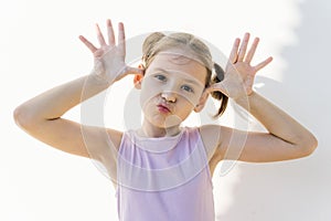 Cute little girl in violet dress make faces against white concrete wall. Joy, childhood