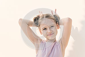 Cute little girl in violet dress make faces against white concrete wall. Joy, childhood