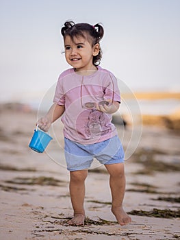 Cute little girl walking on sandy beach, holding bucket and sunglasses. Warm day. Happy childhood. Summer vacation. Holiday