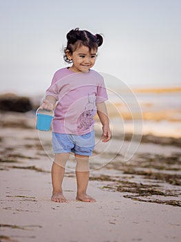 Cute little girl walking on sandy beach and holding bucket. Warm sunny day. Happy childhood. Summer vacation. Holiday concept.