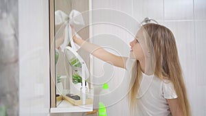 a cute little girl washes sink and the bathroom mirror with a special cleaner.