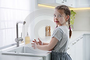 Cute little girl washing hands with liquid soap in kitchen