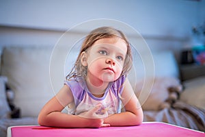 cute little girl watches tv while sitting at the children's table at home. Lifestyle concept