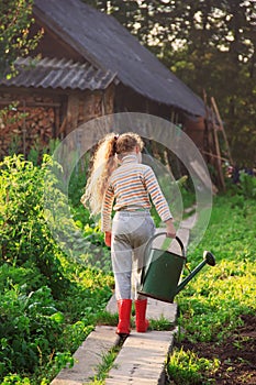 Cute little girl watering plants with watering can in garden. C