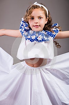 Cute little girl wearing beautiful white and blue dress with matching head band, actively posing for camera, studio