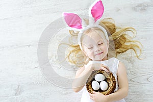 Cute little girl wearing bunny ears playing egg hunt on Easter