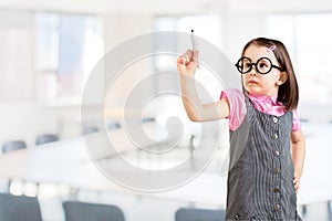 Cute little girl wearing business dress and draws something on virtual screen. Office background.