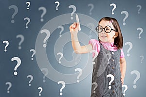 Cute little girl wearing business dress and writing question mark. Blue background.
