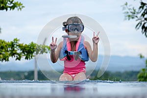 Cute little girl wearing goggles is sitting by the pool preparing for a diving lesson. Happy little girl is swimming and playing