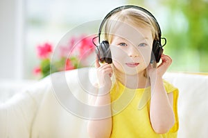 Cute little girl wearing huge wireless headphones. Pretty child listening to the music. Schoolgirl having fun listening to kid`s