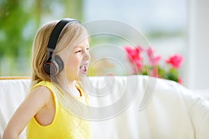 Cute little girl wearing huge wireless headphones. Pretty child listening to the music. Schoolgirl having fun listening to kid`s