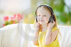 Cute little girl wearing huge wireless headphones. Pretty child listening to the music. Schoolgirl having fun listening to kid`s