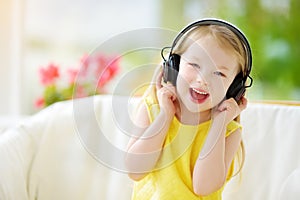 Cute little girl wearing huge wireless headphones. Pretty child listening to the music. Schoolgirl having fun listening to kid`s