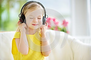 Cute little girl wearing huge wireless headphones. Pretty child listening to the music. Schoolgirl having fun listening to kid`s