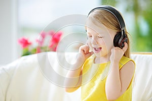 Cute little girl wearing huge wireless headphones. Pretty child listening to the music. Schoolgirl having fun listening to kid`s