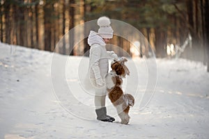 Cute little girl in a white coat with a dog walk in the winter forest. A child is training a dog. Obedience training. Children and