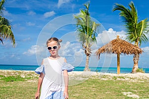 Cute little girl in white dress and hat at beach during caribbean vacation.