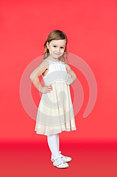 Cute little girl in white dress posing on red background