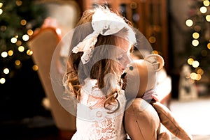 Cute little girl in a white lace dress and a bow on her head holds a teddy bear