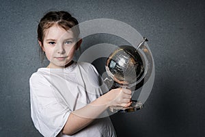 Cute little girl in white t-shirt holding a globe and looking into the frame.