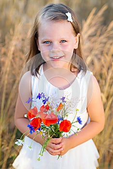 Cute little girl with wild flowers red poppy bouquet in the summer meadow