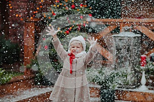 Cute little girl in winter coat and hat catching the snow on a back yard