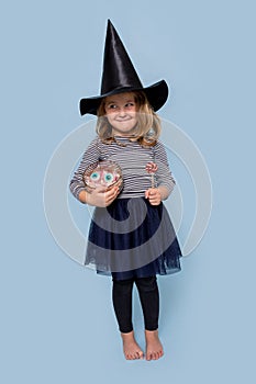 Cute little girl in a witch costume at Halloween holds candy and lollipop