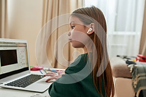 A cute little girl wondering what`s happening on the screen of her laptop during distance education while sitting alone