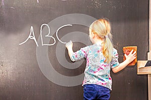 Cute little girl writing ABC on chalkboard
