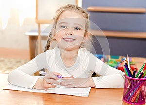 Cute little girl is writing at the desk in preschool